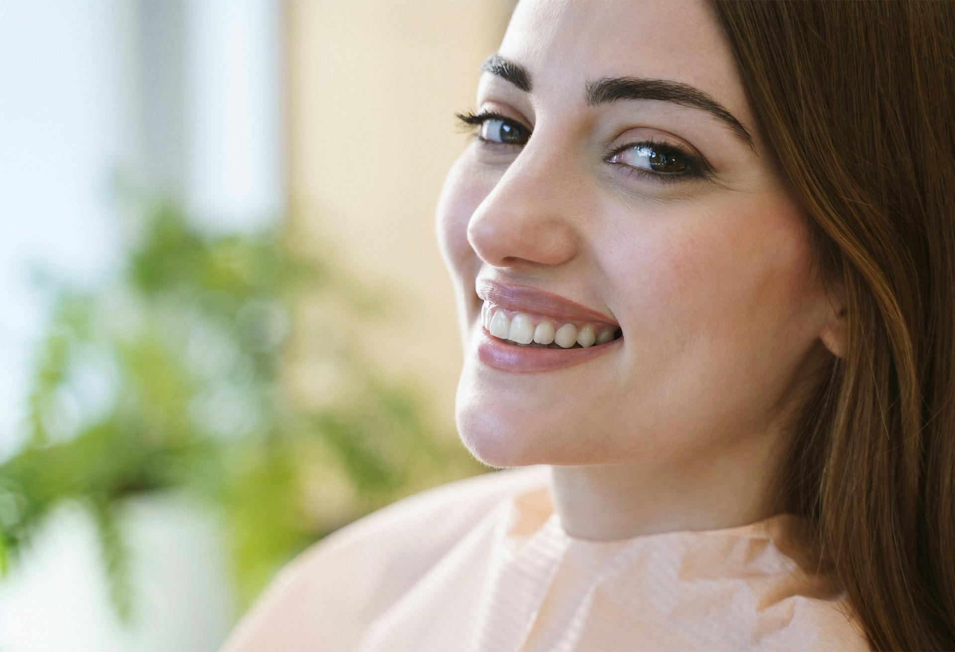 smiling woman with long brown hair and blue eyes looking away