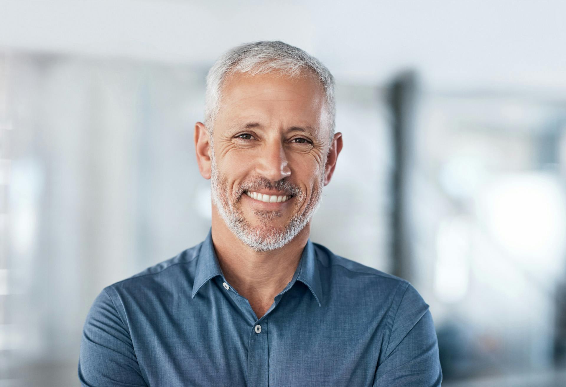 smiling man with grey hair and beard in blue shirt standing in office