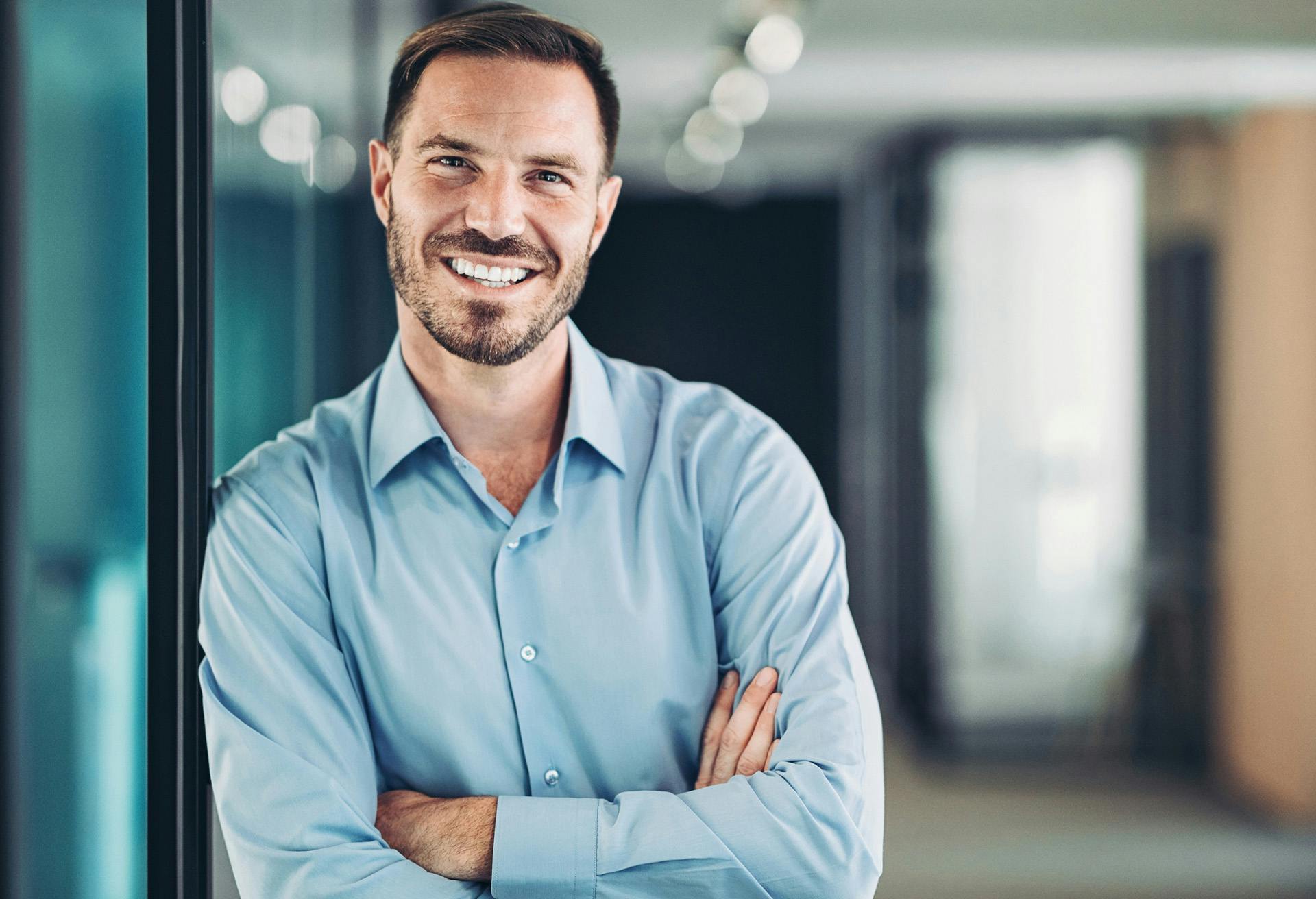 smiling man in blue shirt standing in front of glass wall