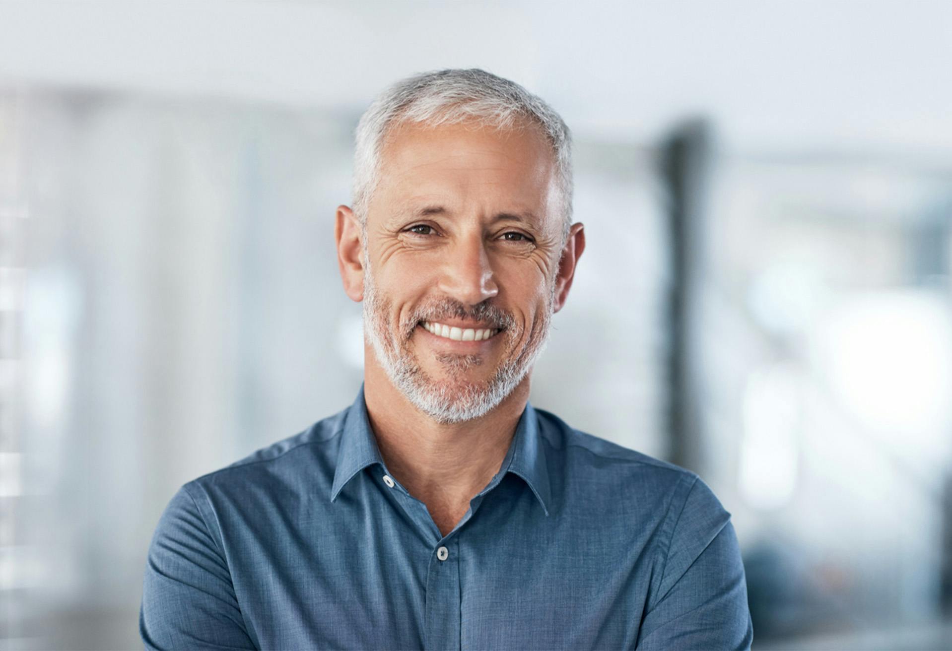 smiling man with grey hair and beard in blue shirt standing in office