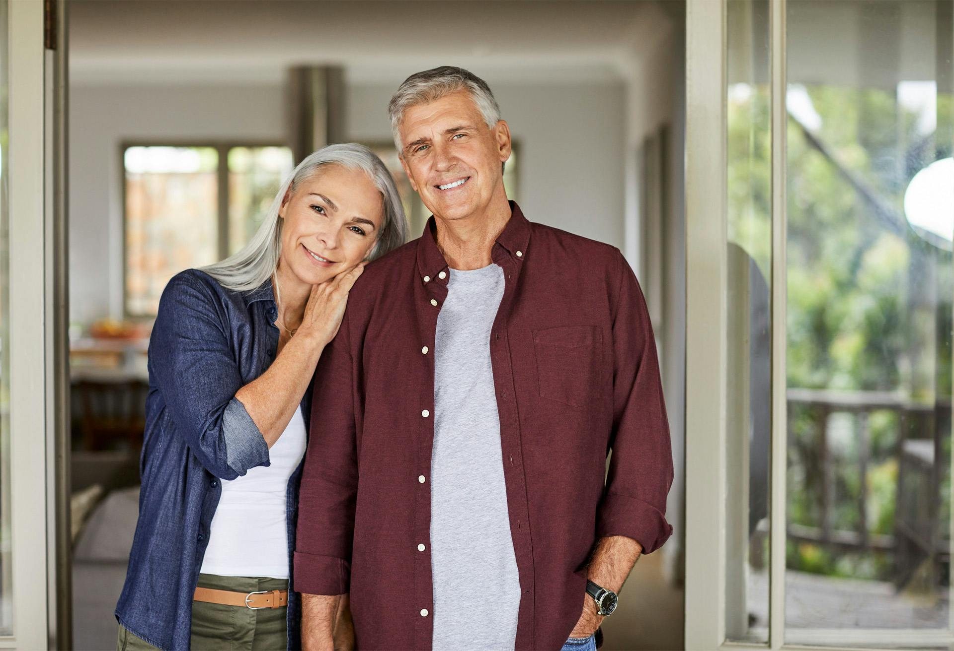 smiling older couple standing in front of open door in home