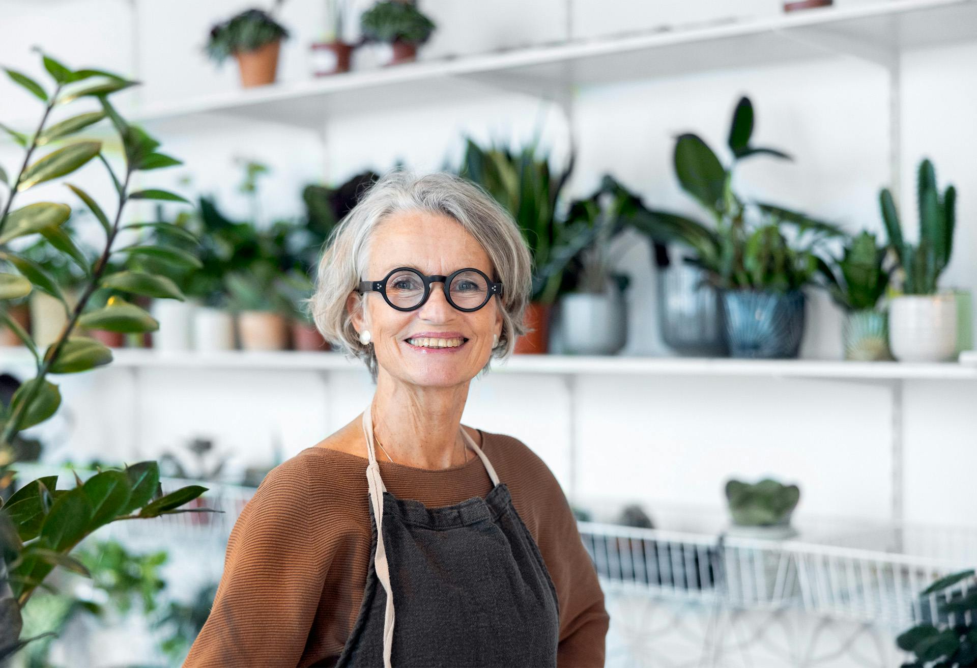 smiling woman in glasses standing in front of a shelf of plants