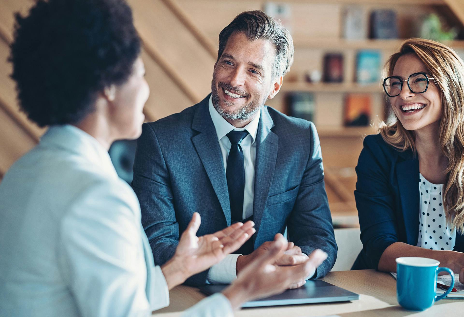 smiling business people sitting at a table with a laptop and a cup of coffee