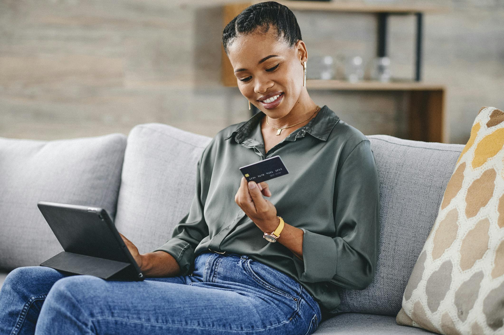 woman sitting on a couch using a laptop and holding a credit card