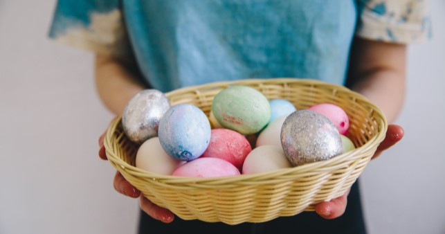 A woman carrying a small basket full of Easter eggs