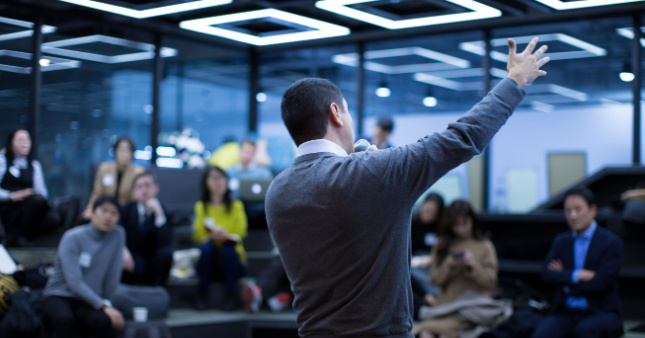 A male manager presenting to a room of male and felame employees