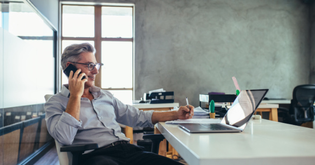 A man at a desk on the phone doing a reference check and making notes