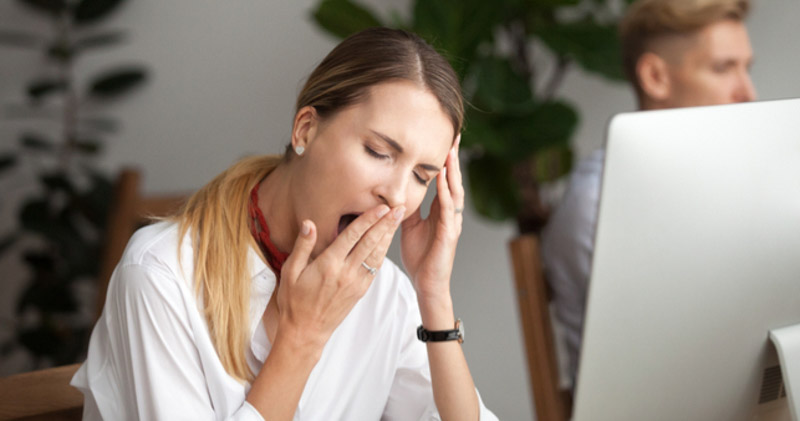 Tired female office worker yawning at desktop computer