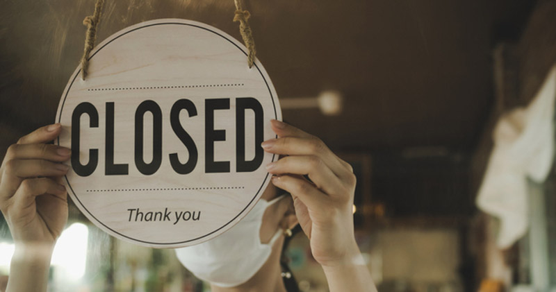 masked shop owner flipping closed sign on window