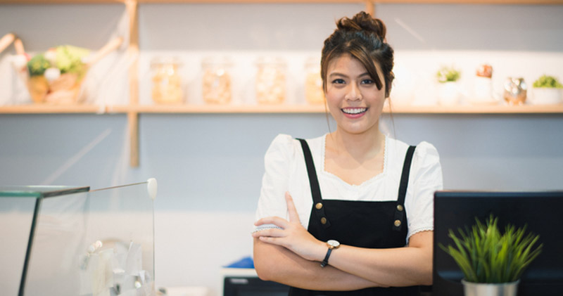 joyful female barista with apron on arms crossed