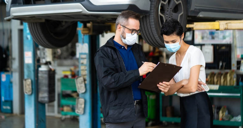 Mechanic and customer looking at checklist with face masks on