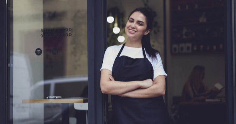 female barista happily leaning outside cafe door