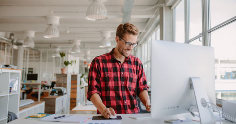 cheerful male office worker using standing desk in sunlit office