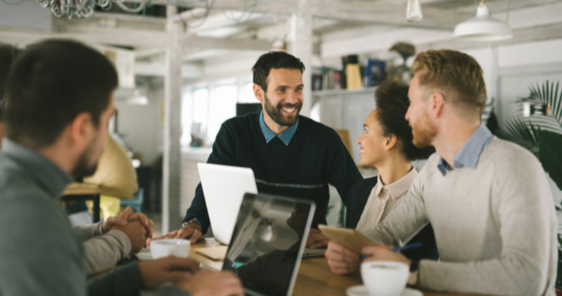 cheerful employees sitting around a lunchroom table conducting a meeting