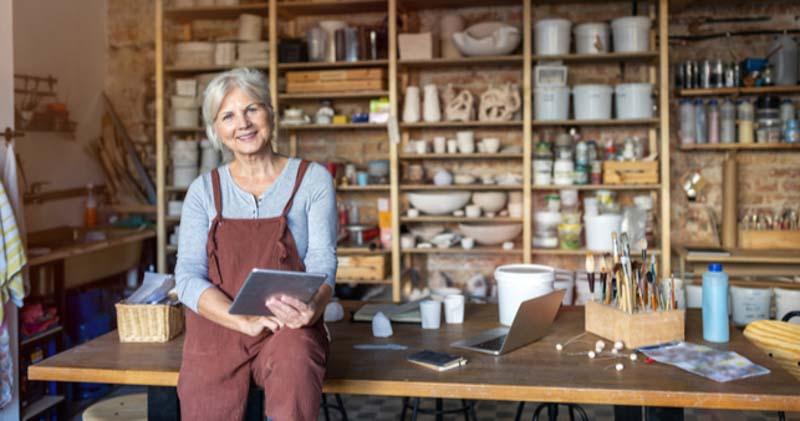 elderly female potter leans on work table in workshop