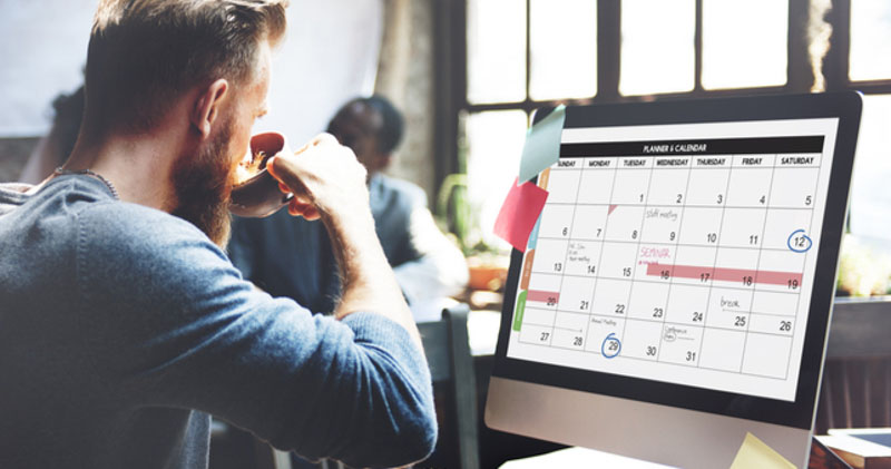 male office worker sits at computer planning calendar