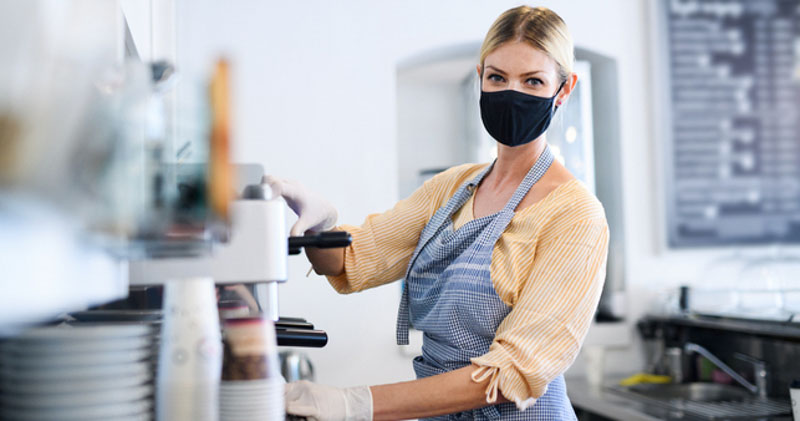 female barista wearing face mask in sunny cafe