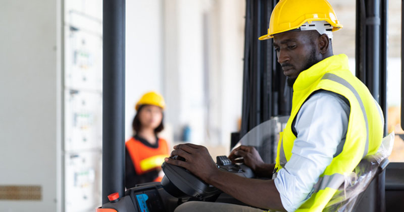 male forklift driver in reflective gear carefully drives forklift