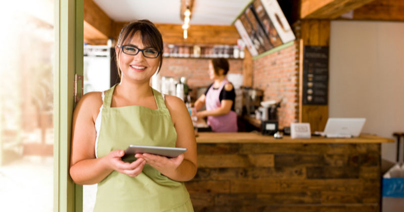 proud female cafe owner leans against door of cafe on sunny day