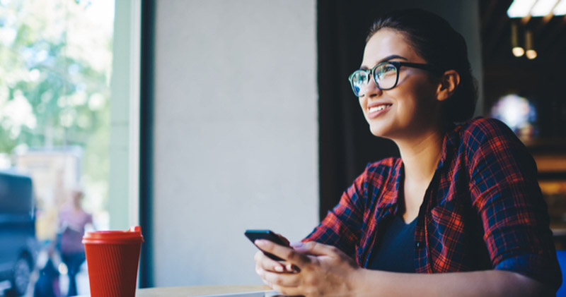 satisfied female on holiday break reads phone in sunny cafe with a coffee