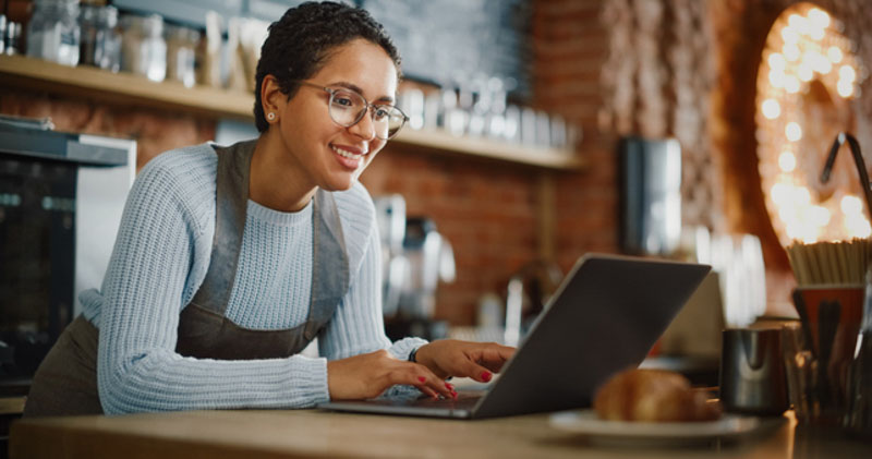 happy young female barista checks laptop in cafe