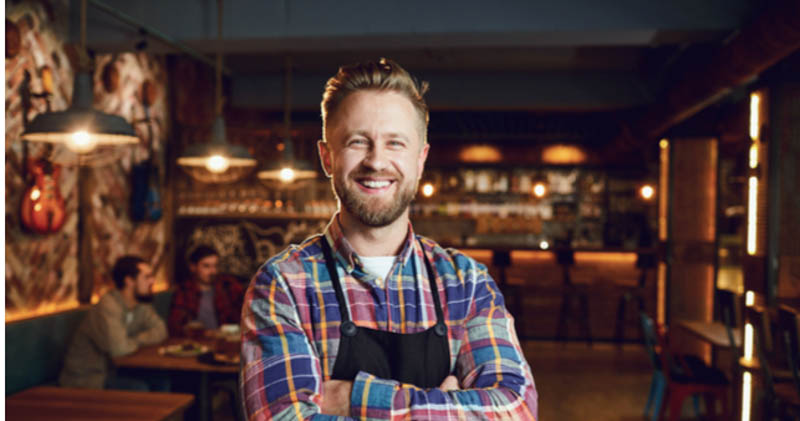 trendy bar owner cheerfully stands in dark bar