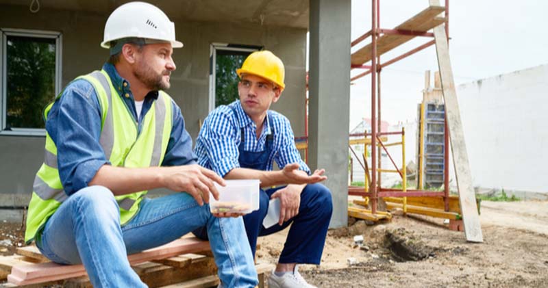two male construction workers chat over lunch on building site