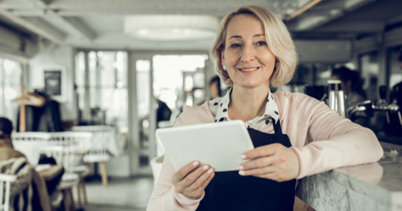 proud female cafe owner leans on counter with tablet