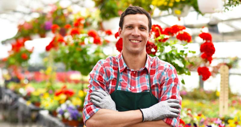 happy male florist crosses arms in greenhouse