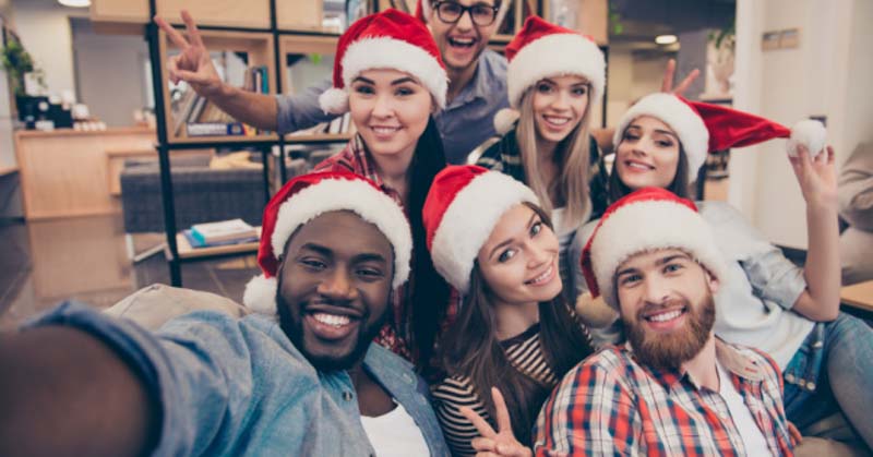 selfie of group of office workers cheerfully wearing santa hats
