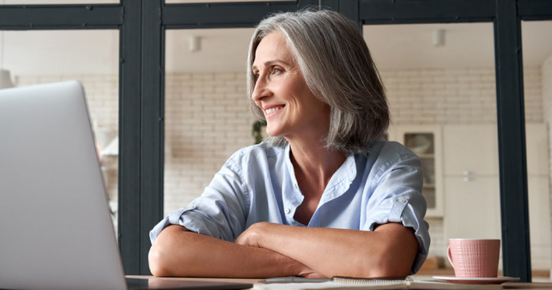 cheerful elderly female employee looks out window in office