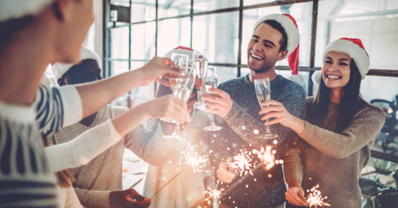cheery office workers celebrate work christmas party with sparklers and santa hats