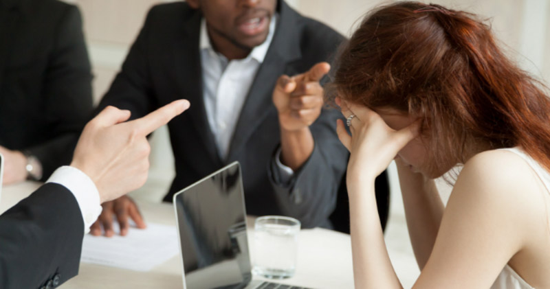 female employee is berated by male colleagues in meeting room
