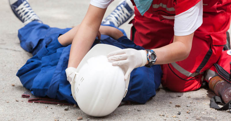 emergency worker assists injured construction worker laying on the ground after accident
