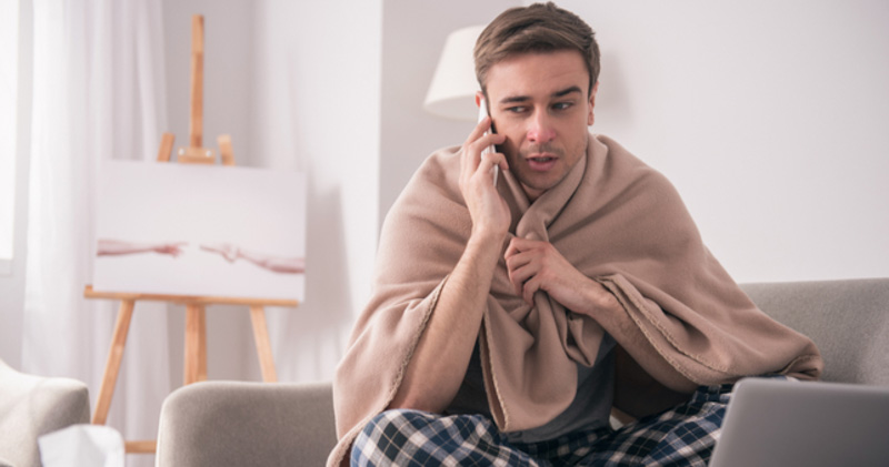 sick man wrapped in blanket phones employer to call in sick