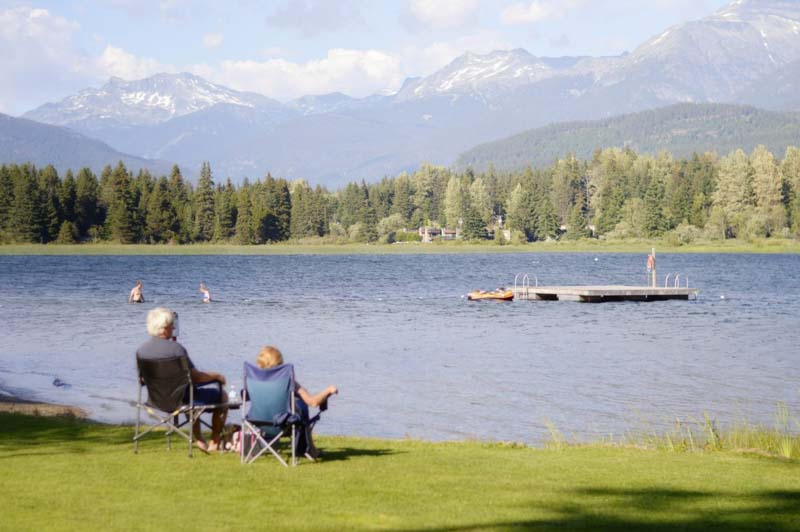 old couple sits by lake on camping chairs