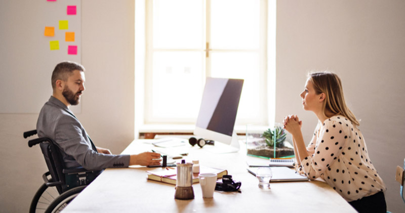 male employee in wheelchair meets with female colleague in sunlit office