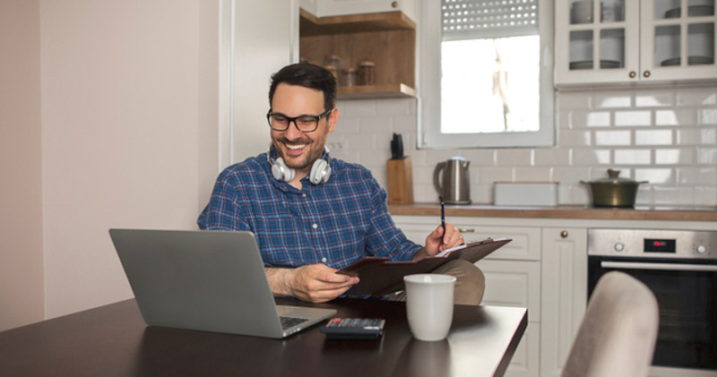 cheerful male remote worker looks at laptop from dining room