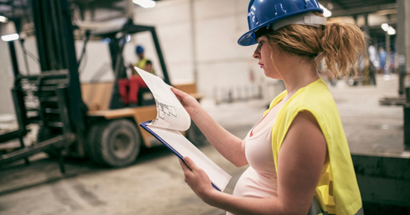 pregnant female warehouse worker reads chart