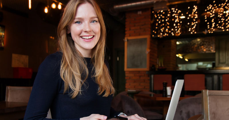happy female employee works on laptop in restaurant