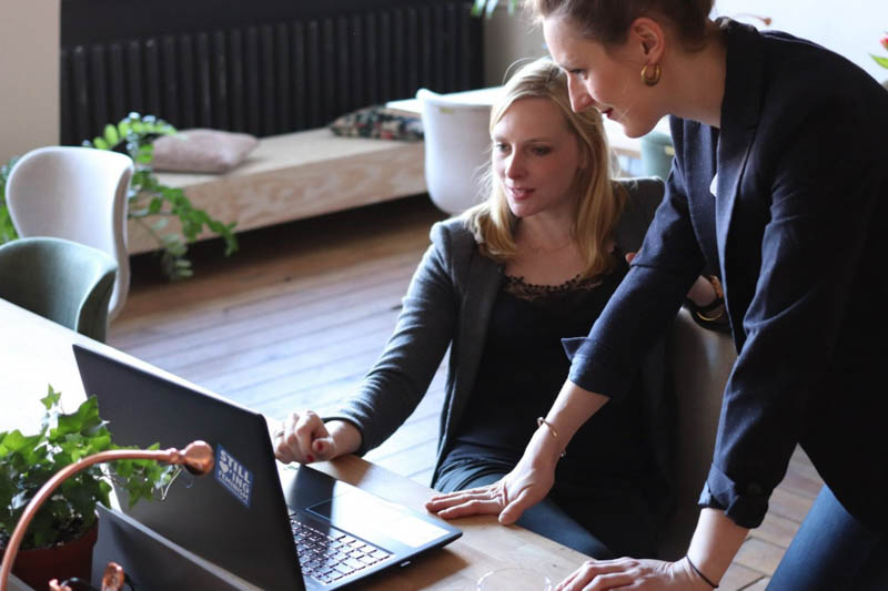 female manager looks over female employee's work on laptop