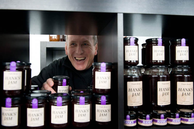 hank's jam owner grins behind shelf of jam jars