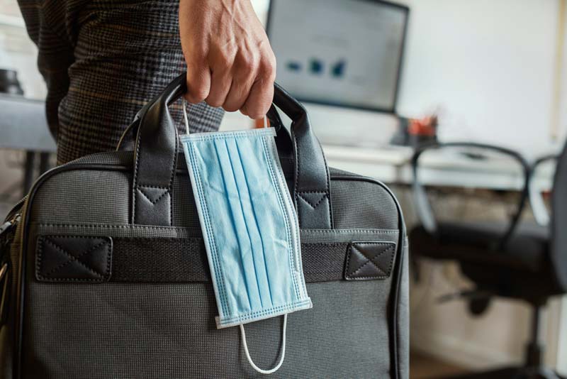 man clutches briefcase and face mask in office