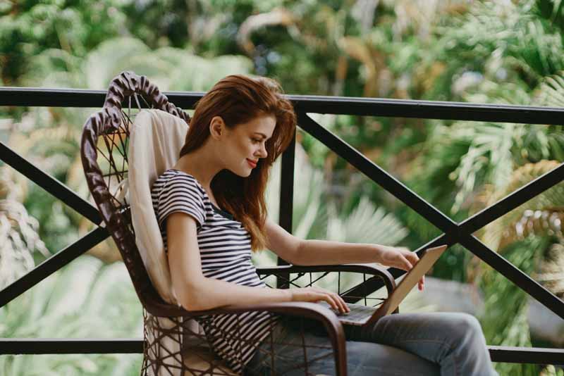 female remote worker reads emails in tropical forest balcony