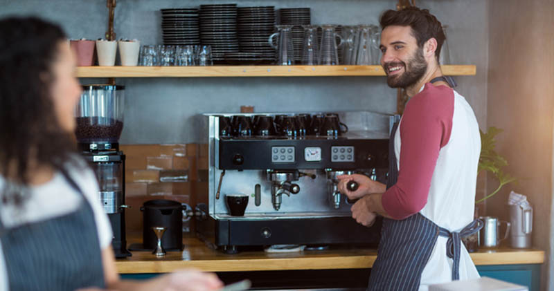 male barista smiles at female coworker in cafe
