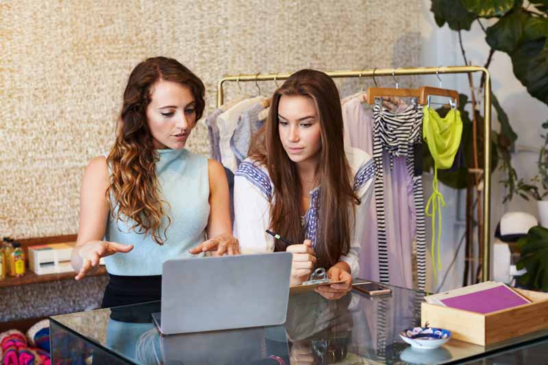 two young fashion employees look at laptop