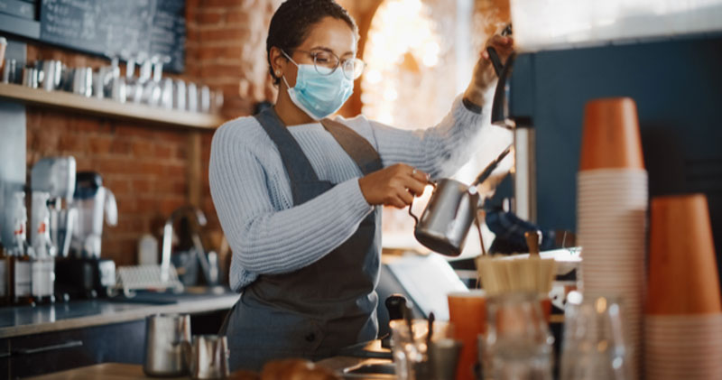 female barista with face mask pours coffee