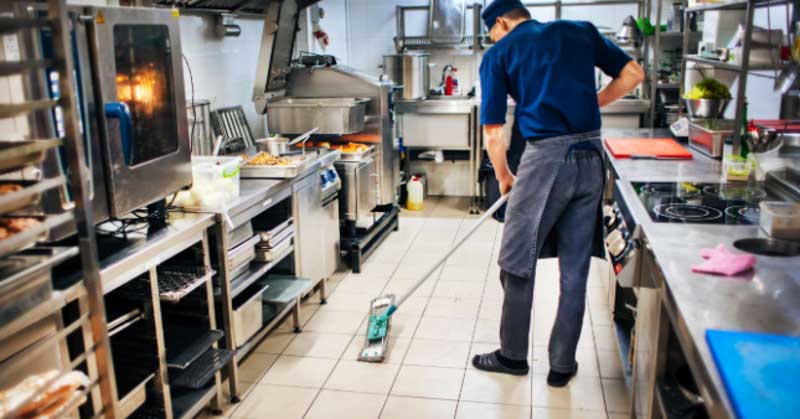 chef sweeps kitchen floor with broom
