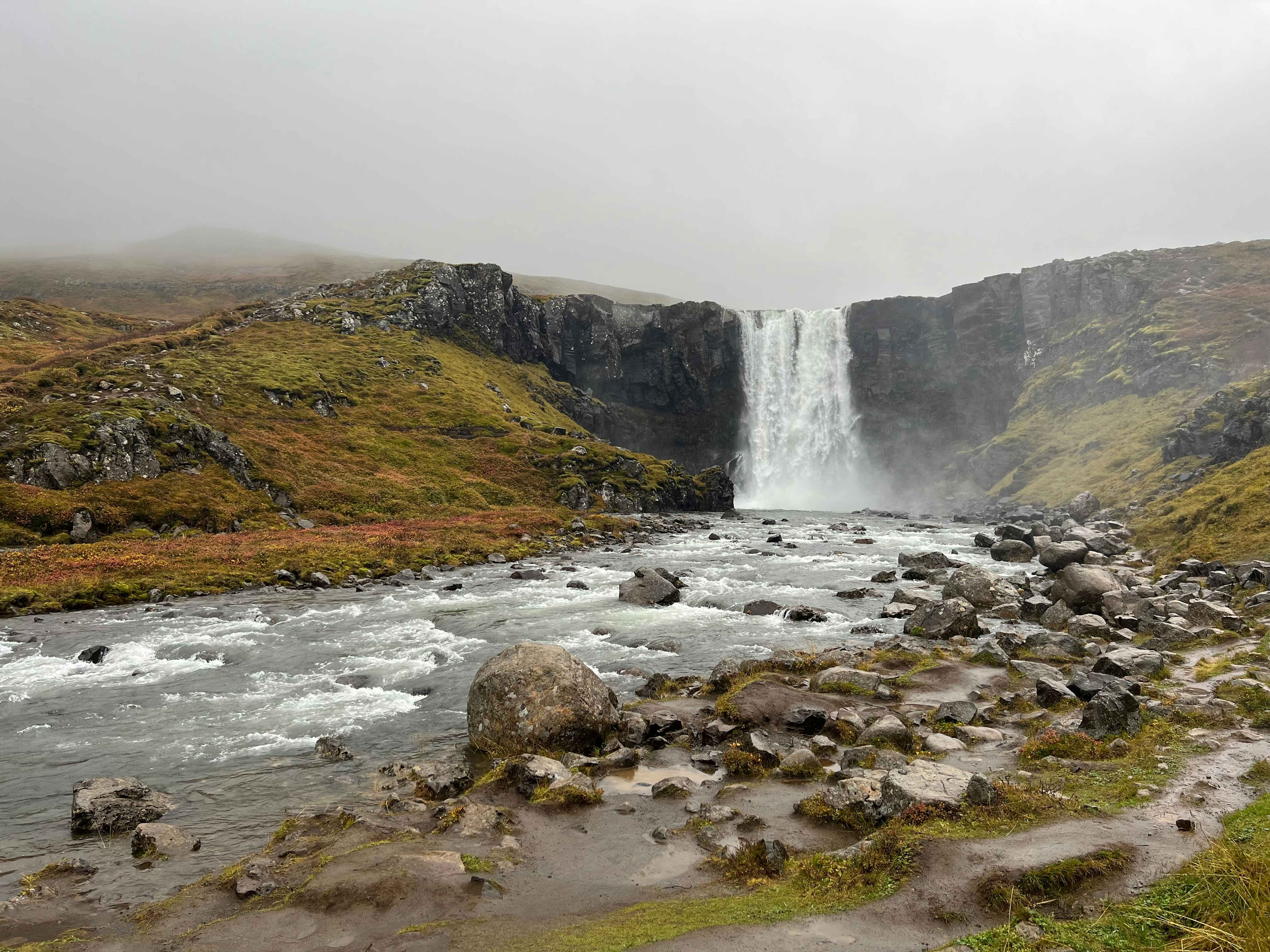 Cascada durante la ruta por la Ring Road Cascada entre paredes de roca y musgo junto a un río, en Islandia.