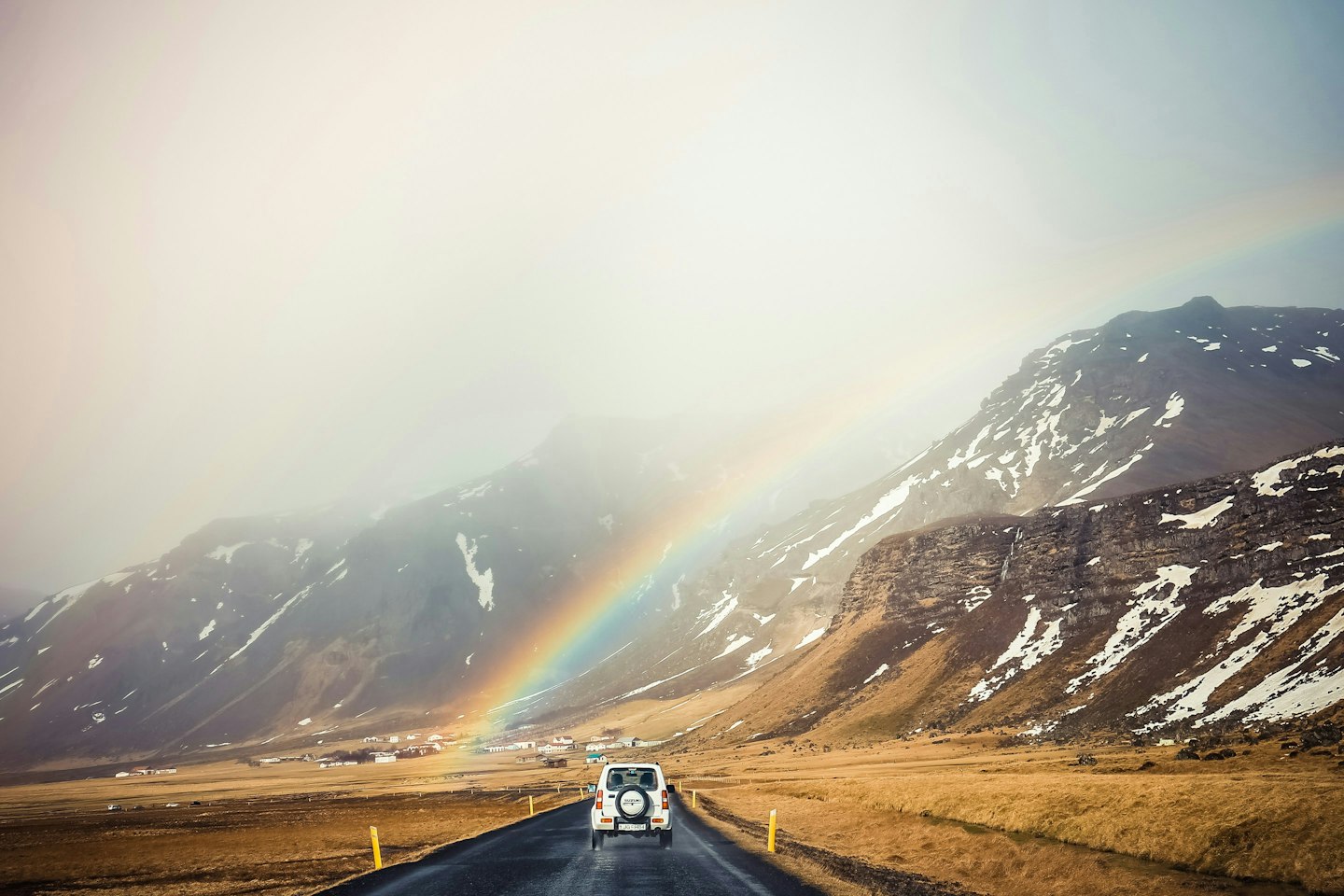 Carretera entre montañas en Islandia Un coche recorre una carretera entre montañas nevadas bajo un arcoíris, en Islandia.